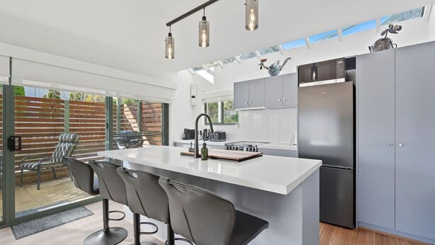 A modern kitchen with a central island, bar stools, a built-in oven, and a stainless steel refrigerator. - Riverview Townhouse Retreat (Lindisfarne)