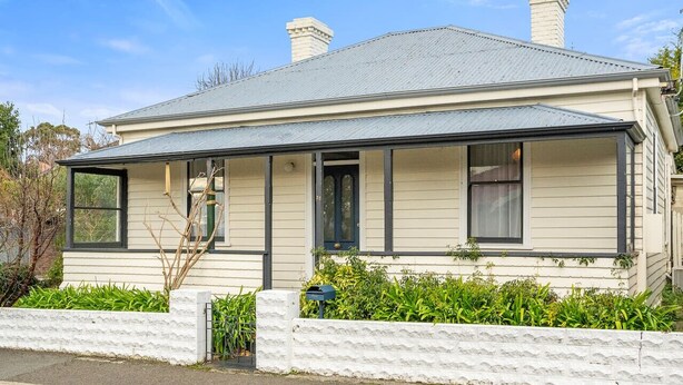 A two-story house with a gabled roof, a front porch, and a white picket fence. - Roope Cottage-Location, Free WiFi & Parking (New Town)