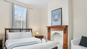 A bedroom with a large bed, a fireplace, a nightstand, a white chair, and a framed picture on the wall. - Roope Cottage-Location, Free WiFi & Parking (New Town)