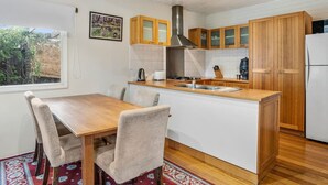 A modern kitchen with wooden cabinets, a central island, and a dining area with chairs. - Roope Cottage-Location, Free WiFi & Parking (New Town)