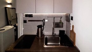 A compact kitchen with a dark countertop, a stainless steel sink, and a kettle. - Modern One-Bedroom Apartment in Kypseli - 1000 Mbps Fiber Wi-Fi (Athina)