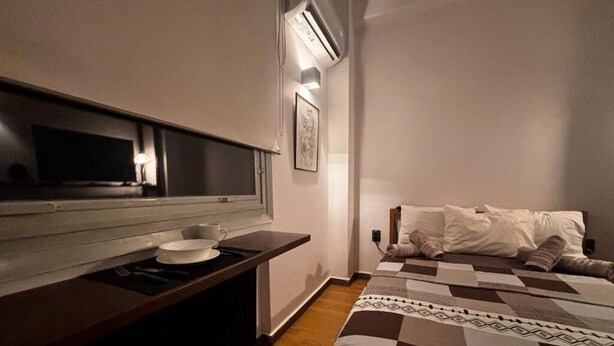 A hotel room with a bed, a desk with a chair, a television, and an air conditioning unit. - Modern One-Bedroom Apartment in Kypseli - 1000 Mbps Fiber Wi-Fi (Athina)