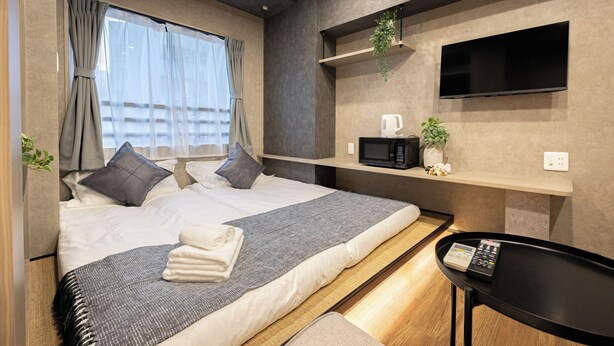 A modern hotel room with a bed, bedside table, TV, and a small shelf with a plant. - A 5-minute walk from Yoyogi Station on the JR Yamanote Line; an apartment for 3 people (渋谷区)