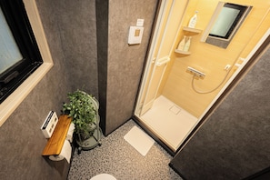 Ein kleines Badezimmer mit Dusche, Toilette, einer Sitzbank und einem Blumentopf.