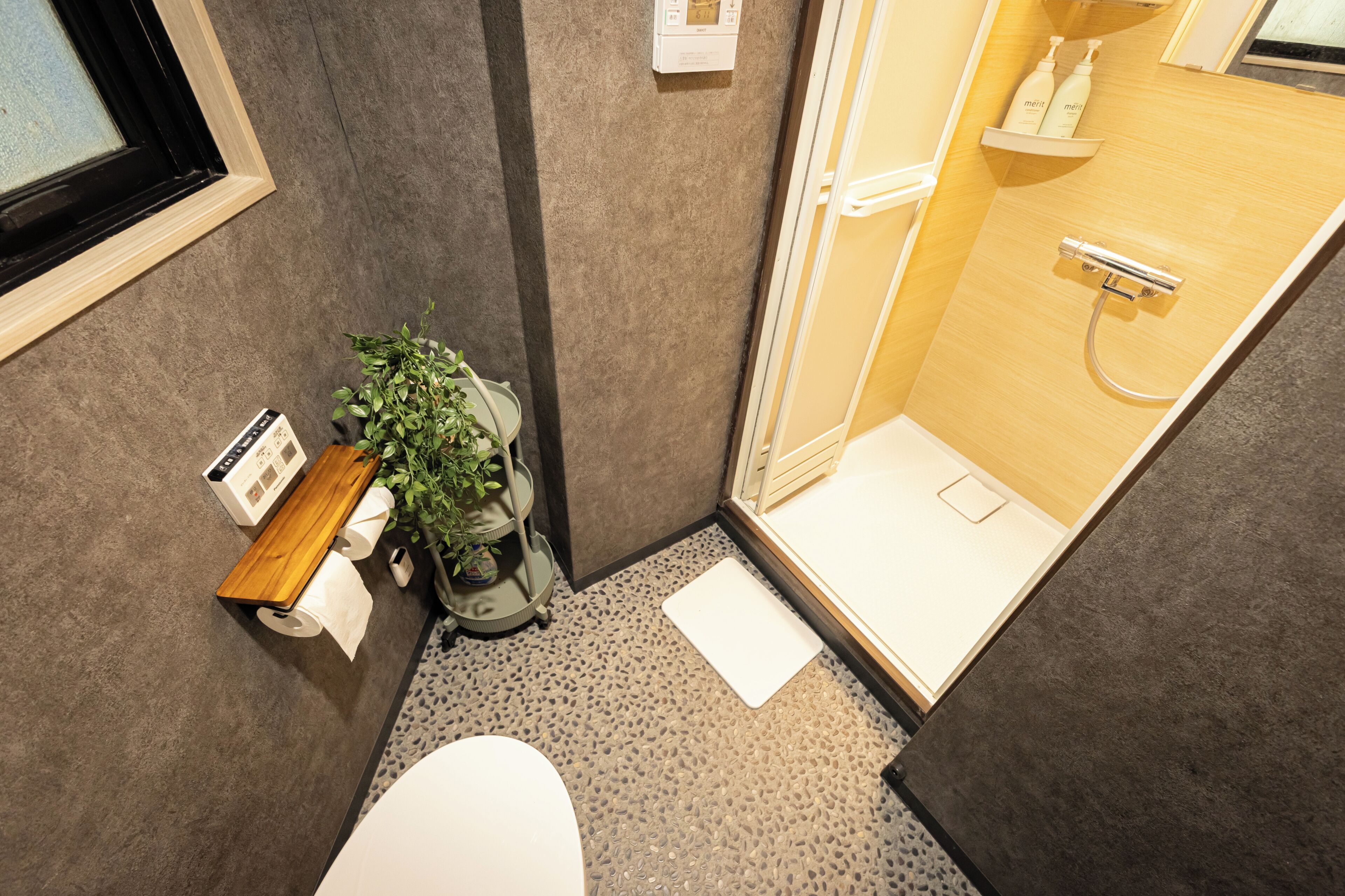 A bathroom with a shower, toilet, and a small shelf with toiletries.