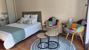 A bedroom with a bed, two chairs, a small table, a coffee maker, and a patterned rug.