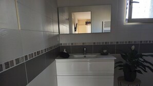 A bathroom with a white vanity, a mirror, a towel, a soap dispenser, a kettle, and a potted plant.