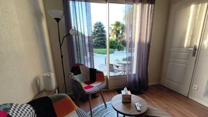 A living room with a sofa, a chair, a round table, and a view of the outdoors through a glass door.