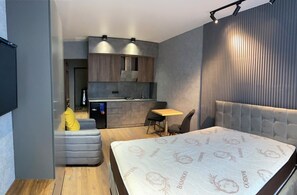 Ein gemütlicher Raum mit einem Bett, einer kleinen Küchenzeile, einer Sitzecke und einem an der Wand befestigten Fernseher.