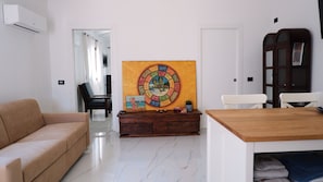 A living room with a sofa, a dining table, a cabinet, and a colorful artwork on the wall. - Sardinia Sea Relax with a Private Hot Tub Near the Beach (Quartu Sant'Elena)