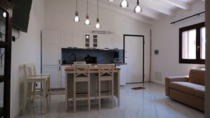 Una cocina con armarios blancos, una mesa de comedor de madera con sillas, una cafetera y luces colgantes.