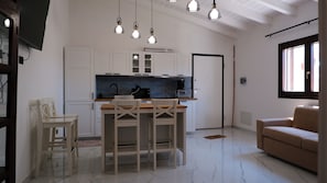 A kitchen with white cabinets, a wooden dining table with chairs, a coffee machine, and pendant lights. - Sardinia Sea Relax with a Private Hot Tub Near the Beach (Quartu Sant'Elena)