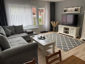 A modern living room with a grey sofa, a white coffee table, a TV on a cabinet, and a patterned rug. - Cozy Vacation Rental in Butjadingen in a Quiet Setting (Butjadingen)
