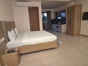 A bedroom with a bed, a wooden wardrobe, a kitchenette, and an air conditioning unit. - Star Residency near Medanta Hospital (Gurugram)