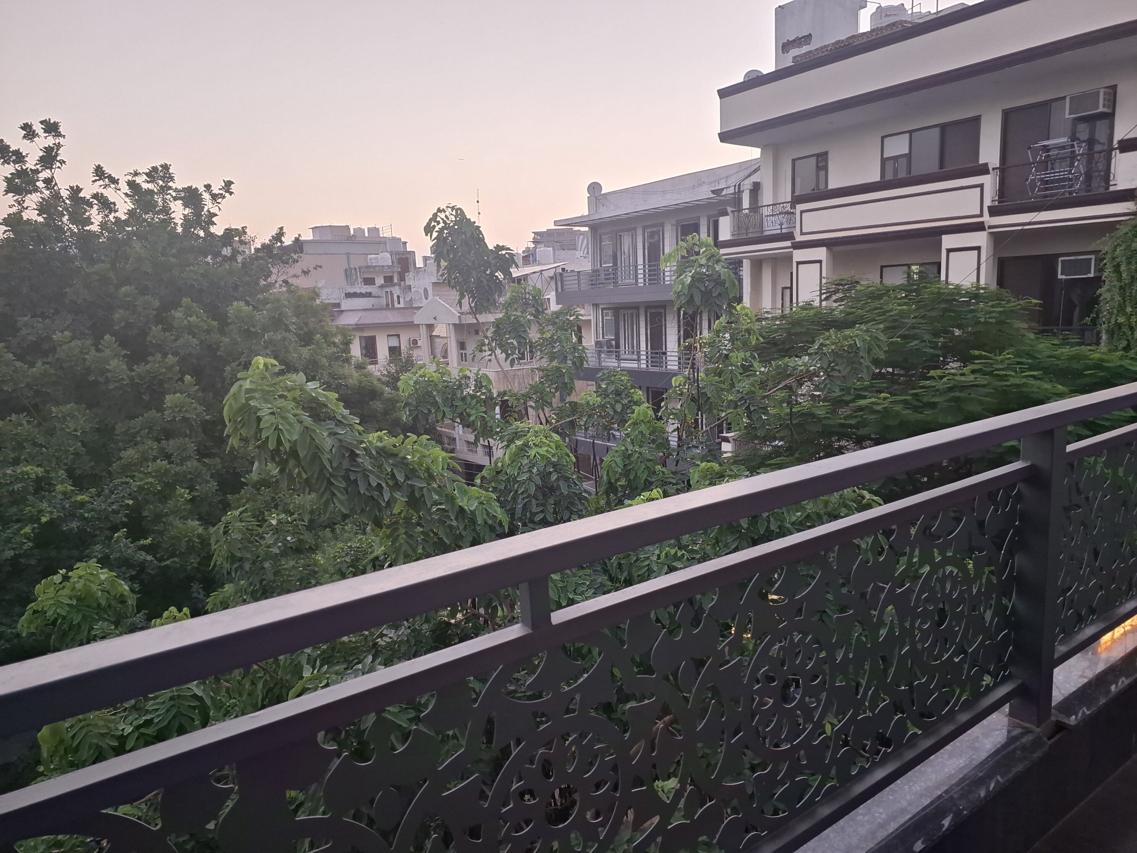 A residential area with modern buildings, a balcony with decorative railing, and dense greenery.