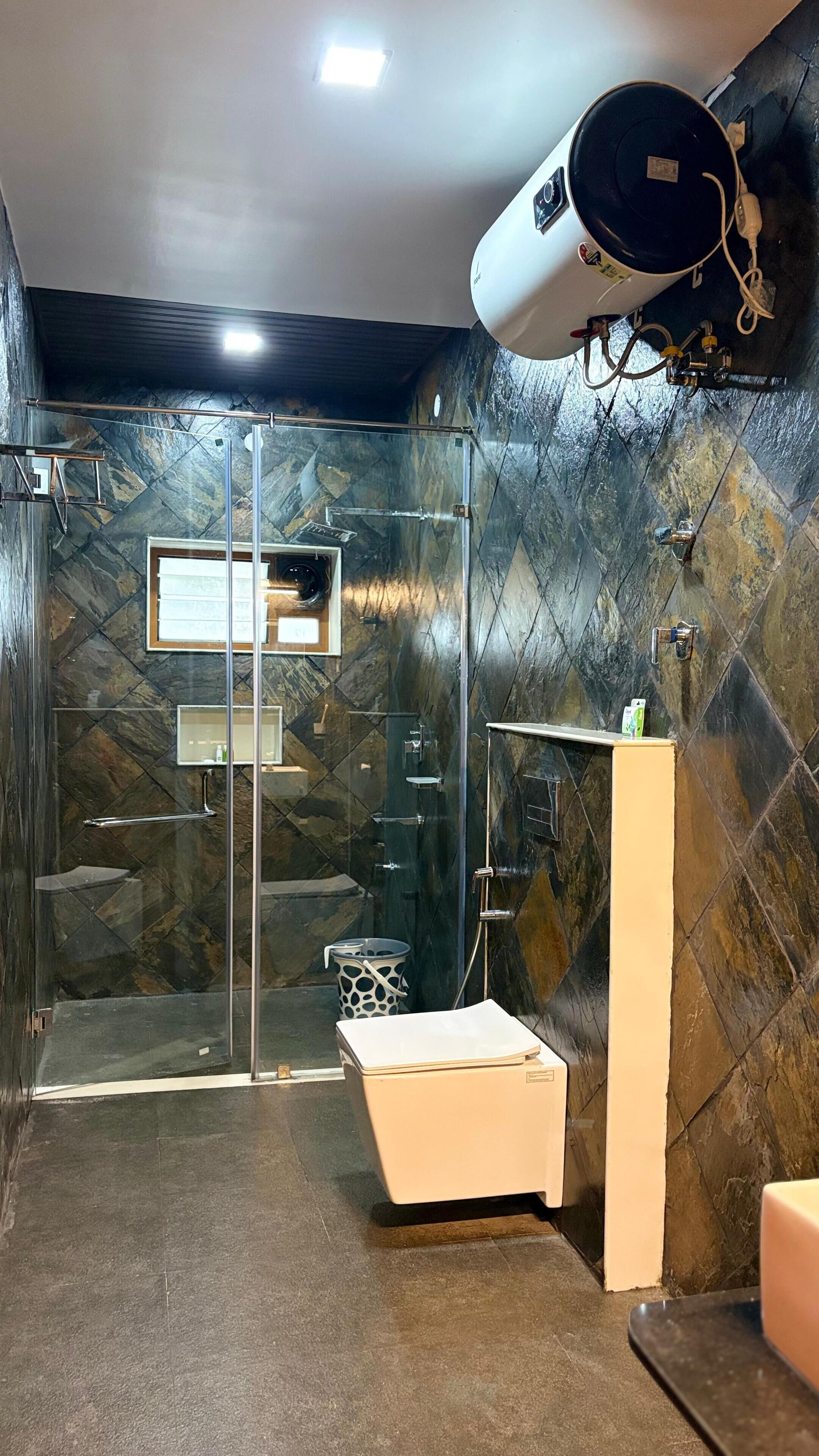 A modern bathroom with a glass-enclosed shower, a white pedestal sink, and a marble-patterned wall.