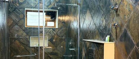A modern bathroom with a glass-enclosed shower, a white pedestal sink, and a marble-patterned wall.