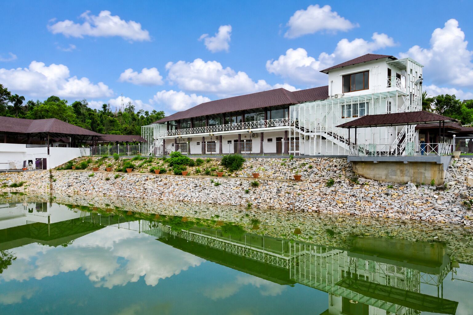 Un edificio moderno con un ampio balcone, un muro di sostegno in pietra e una superficie d'acqua riflettente.