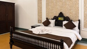A bedroom with a large wooden bed, a nightstand, a wardrobe, and patterned wallpaper.