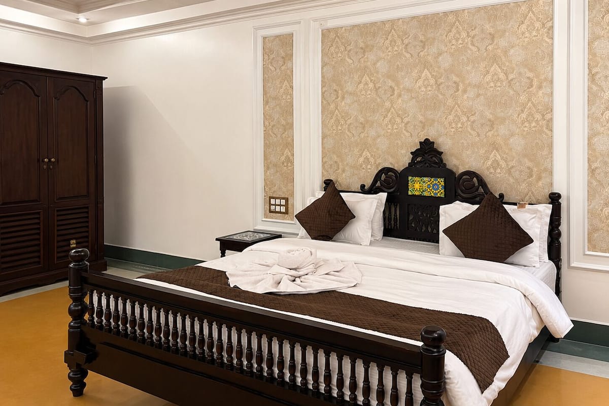 A bedroom with a large wooden bed, a nightstand, a wardrobe, and patterned wallpaper.