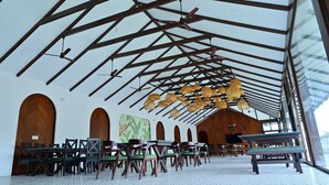 A spacious hall with a high ceiling, wooden beams, and a series of tables and chairs arranged for dining.