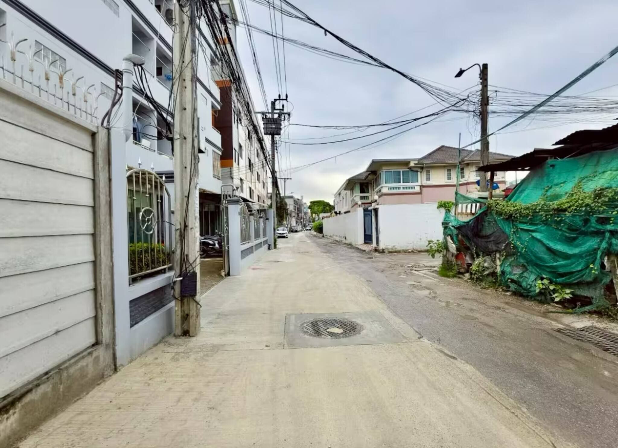 A narrow urban street with residential buildings, a manhole cover, and overhead power lines.