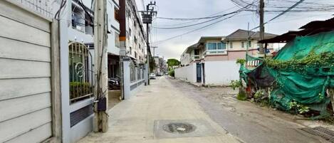 A narrow urban street with residential buildings, a manhole cover, and overhead power lines.