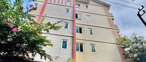 A multi-story building with a flat roof, a red vertical feature, and a gated entrance.