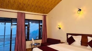 A bedroom with a wooden ceiling, a large bed, a window with curtains, and a view.