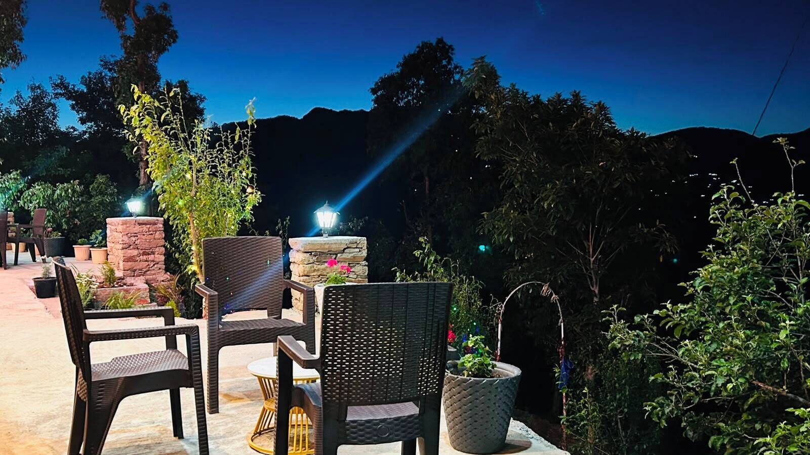 An outdoor seating area with wicker chairs and a stone fireplace, surrounded by greenery.
