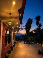 A covered outdoor area with hanging lights, potted plants, and a view of the sky.