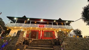 A building with a sign reading 'Radhika Retreat,' featuring a balcony, stairs, and a stone facade.