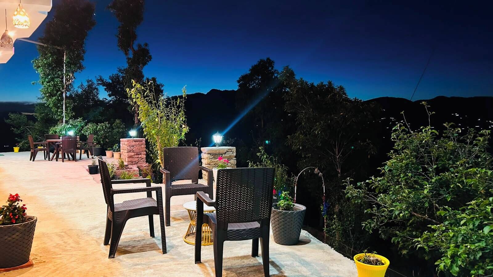 Un espace extérieur aménagé avec des chaises et des tables, entouré de verdure et offrant une vue sur les montagnes.
