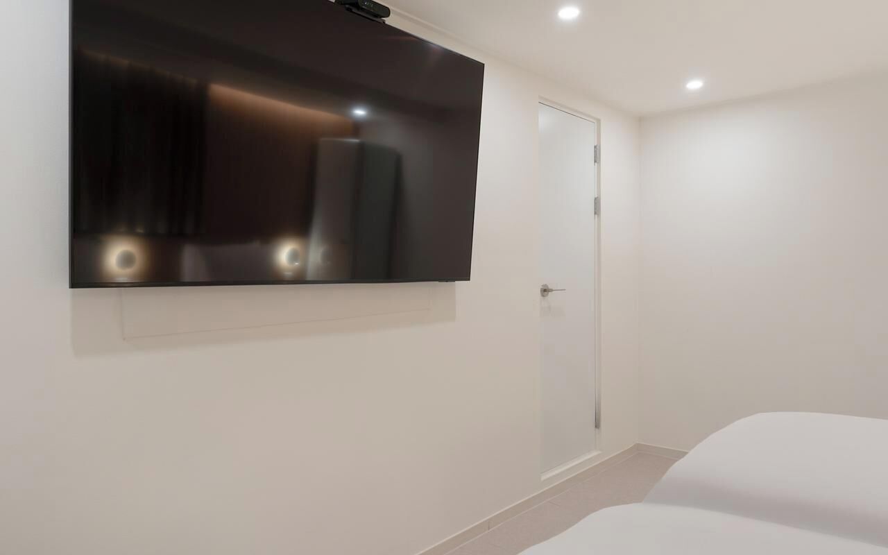 A modern hotel room with a large flat-screen TV mounted on the wall, a door, and a bed.