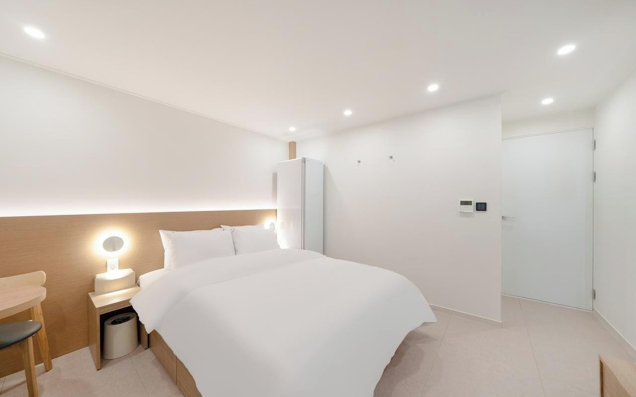 Ein modernes Hotelzimmer mit einem großen Bett, einem Nachttisch mit Lampe, einem kleinen Schreibtisch und einem Kleiderschrank.
