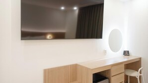 Habitación moderna con un espejo grande, un escritorio de madera, una silla y un televisor montado en la pared.