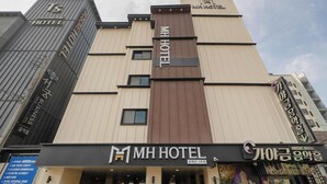 Un edificio de hotel con un llamativo letrero 'MH HOTEL', un salón de música y varios balcones.
