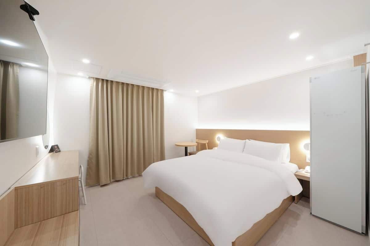 Una habitación de hotel moderna con cama, mesitas de noche, escritorio, espejo y armario.