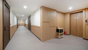 Un pasillo de hotel con puertas de madera, un extintor y una pantalla digital en la pared.