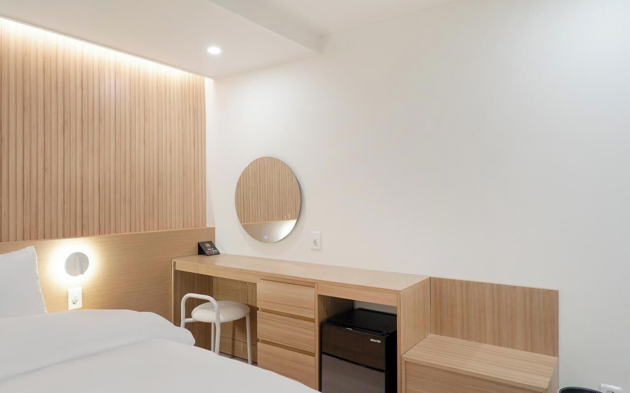 Habitación de hotel moderna con cama, escritorio con silla, espejo redondo y armario empotrado.