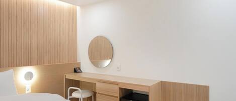 Habitación de hotel moderna con cama, escritorio con silla, espejo redondo y armario empotrado.