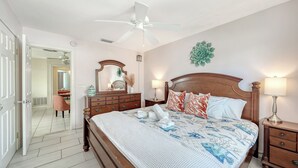 Una habitación de hotel con una cama de madera, un ventilador de techo, una mesita de noche con lámpara y un espejo en la pared.