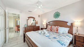 A hotel room with a wooden bed, a ceiling fan, a nightstand with a lamp, and a mirror on the wall. - 2R Lido Key - Steps to Beach, Walk to St. Armand's (Sarasota)