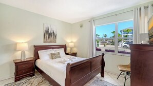 Une chambre d’hôtel avec un lit, deux tables de chevet avec des lampes, un tableau au mur, une fenêtre donnant sur l’extérieur et une chaise.
