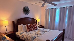 A neatly made bed with a floral bedspread, two bedside lamps, a ceiling fan, and a window with curtains. - 1R Lido Key - Steps to Beach, Walk to St. Armand's (Sarasota)