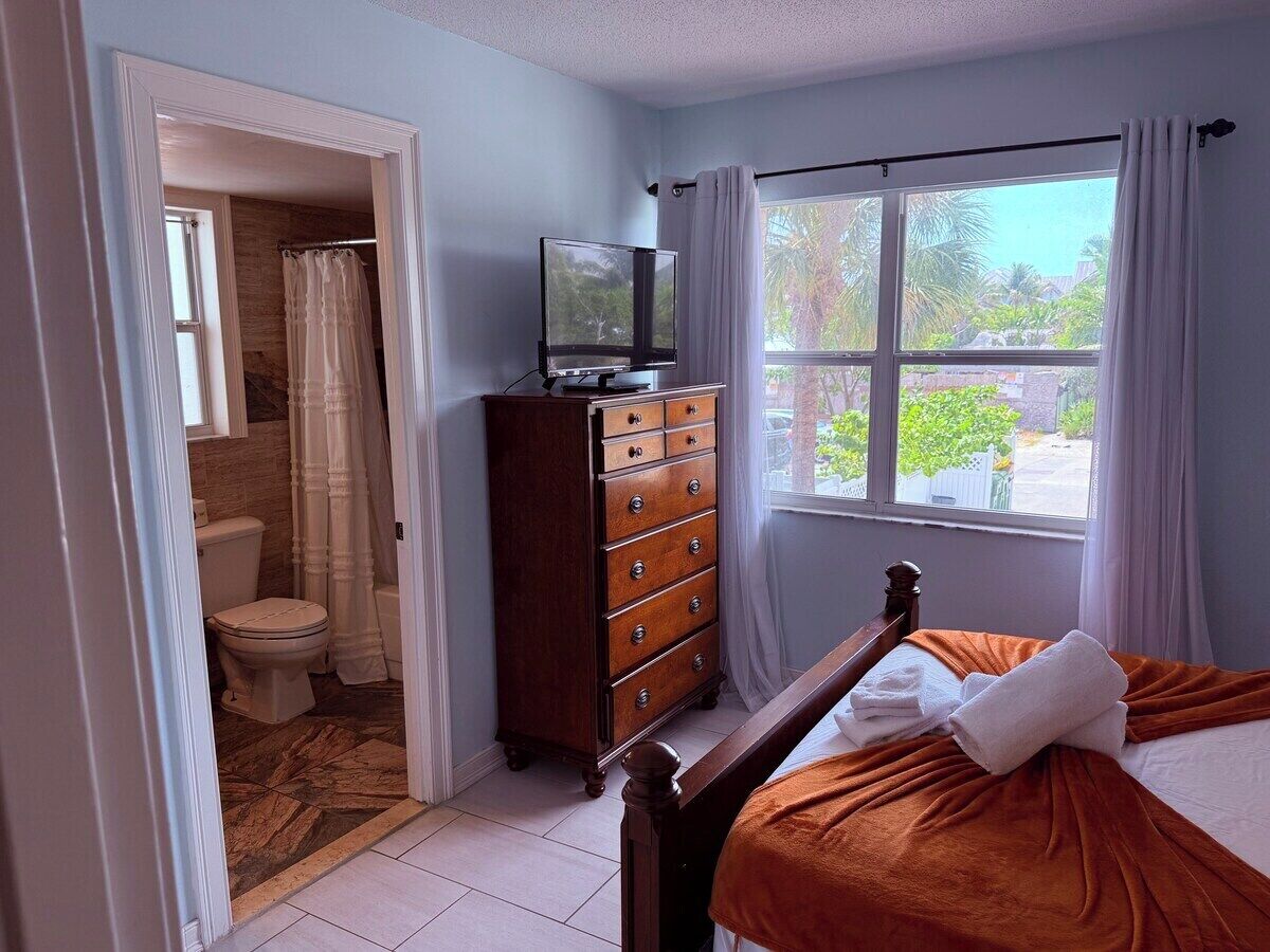 A bedroom with a bed, a dresser, a television, and a window with curtains.