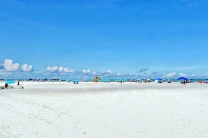 En strand med vit sand, parasoller och ett badvakts torn.