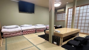 Una habitación con esteras de tatami, una mesa baja, futones y una televisión.
