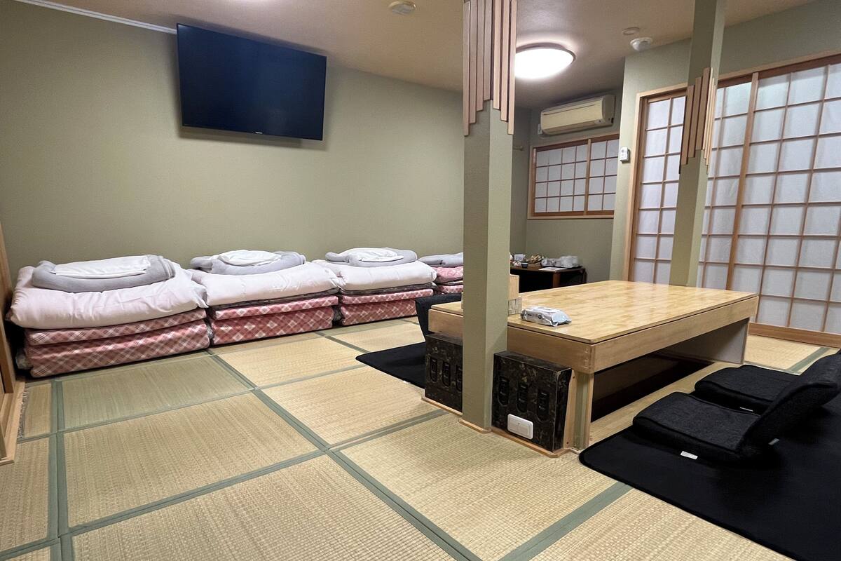 Una habitación con esteras de tatami, una mesa baja, futones y una televisión.