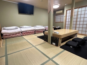 Una habitación con esteras de tatami, una mesa baja, futones y una televisión.